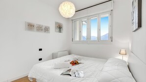 En snyggt bäddad säng med ett vitt täcke, ett fönster med utsikt över bergen och en vägg med tre inramade konstverk.