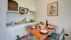 A modern kitchen with white cabinets, a microwave, and a dining area with a wooden table set for two. - Porto Letizia P12, Porlezza, Italy (Porlezza)