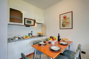 Una cocina moderna con armarios blancos, un microondas y un comedor con mesa de madera dispuesta para dos.