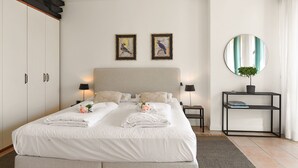 A neatly made double bed with white linens, two framed wall art pieces, a round mirror, and a small side table with a plant. - Porto Letizia P11, Porlezza, Italy (Porlezza)