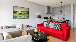 A living room with a red sofa, a white sofa, and a black coffee table. There is a painting on the wall and a kitchen in the background. - Porto Letizia P11, Porlezza, Italy (Porlezza)