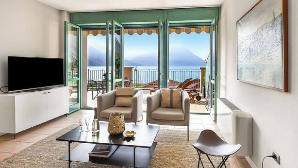 A living room with a large TV, two armchairs, a coffee table, and a view of the sea through glass doors. - Porto Letizia P11, Porlezza, Italy (Porlezza)