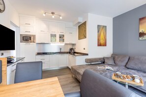 A modern kitchen with white cabinets, a built-in oven, and a dining area with a wooden table and grey chairs. - Porto Letizia Iris 2, Porlezza, Italy (Porlezza)