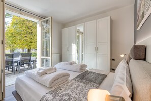 A bedroom with a bed, a bedside table, a chair, and a view of an outdoor area with a table and chairs. - Porto Letizia Iris 2, Porlezza, Italy (Porlezza)