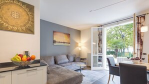 Een moderne woonkamer met een grijze bank, een eettafel met stoelen, een fruitschaal en een schilderij aan de muur.