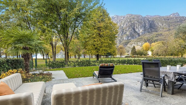 Een terras met een tafel en stoelen, omgeven door groen en uitzicht op bergen.