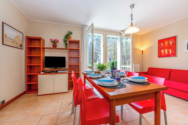 Uma área de refeições com uma mesa de madeira, cadeiras vermelhas e uma televisão em um móvel.
