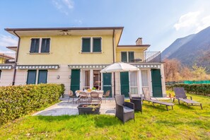 A two-story building with a patio area, outdoor seating, and a view of a mountain. - Porto Letizia Dalia 1, Porlezza, Italy (Porlezza)