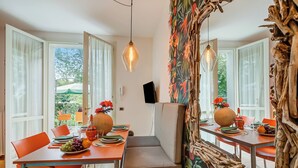 A dining area with a table set for two, featuring orange chairs, a bench, and a view of the outdoors. - Porto Letizia Begonia 3, Porlezza, Italy (Porlezza)