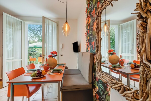 A dining area with a table set for two, featuring orange chairs, a bench, and a view of the outdoors.