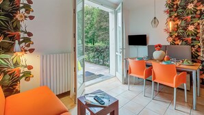 A modern dining area with a glass door leading to a garden, orange chairs, a table with a vase, and a flat-screen TV. - Porto Letizia Begonia 3, Porlezza, Italy (Porlezza)