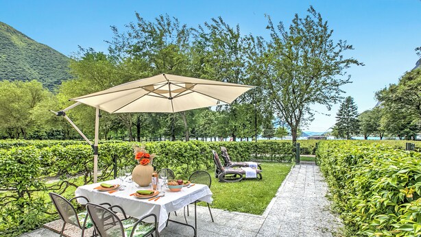 An outdoor dining area with a table set for two, surrounded by greenery and a view of the mountains. - Porto Letizia Begonia 3, Porlezza, Italy (Porlezza)