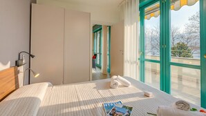A hotel room with a bed, a nightstand, a lamp, a window with curtains, and a view of the outside.