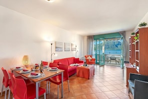 A dining area with a red table set for four, a red sofa, and a balcony with a view. - Porto Letizia P13 B1, Porlezza, Italy (Porlezza)