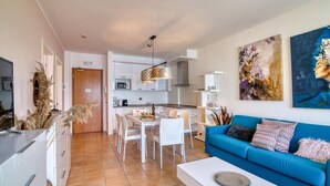 A modern living room with a blue sofa, white dining table, and a kitchen in the background. - Porto Letizia T12 B1, Porlezza, Italy (Porlezza)