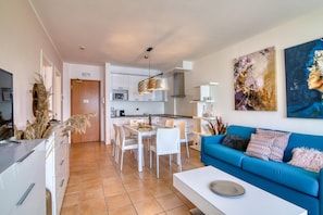 A modern living room with a blue sofa, white dining table, and kitchen in the background. - Porto Letizia T12 B1, Porlezza, Italy (Porlezza)