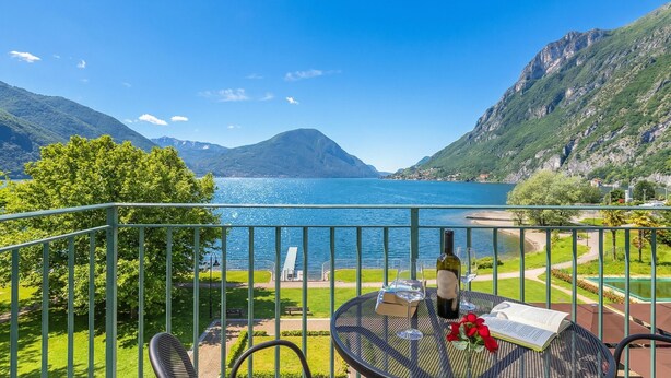A balcony with a table, a chair, a bottle of wine, and an open book. - Porto Letizia T12 B1, Porlezza, Italy (Porlezza)