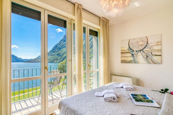 Une chambre d’hôtel avec une grande fenêtre, un lit avec des serviettes soigneusement pliées, un tableau encadré au mur et un balcon avec une chaise.