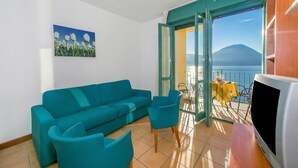 A living room with a sofa, chairs, a TV, a painting, and a balcony with a table and chairs. - Porto Letizia T11, Porlezza, Italy (Porlezza)