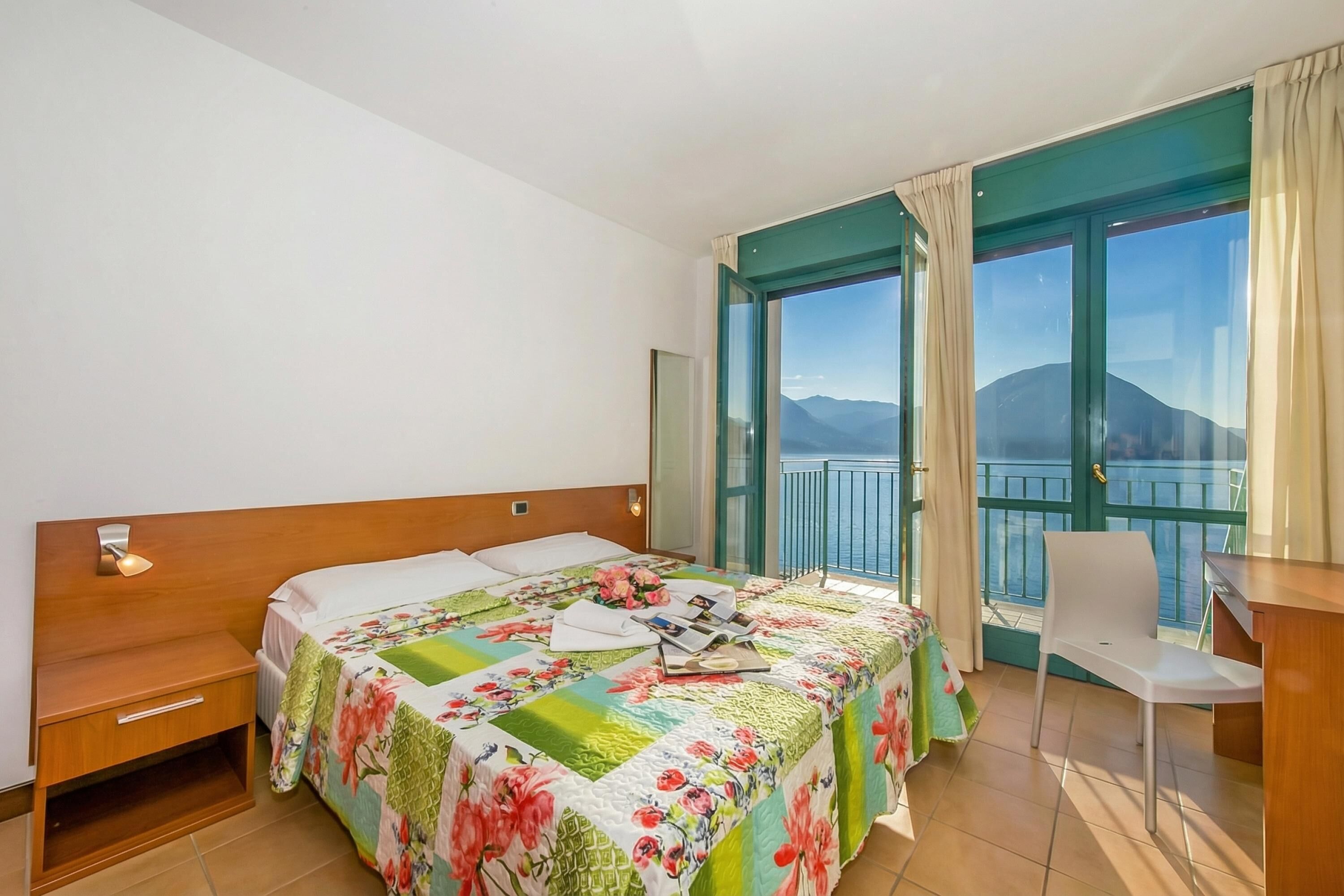 Une chambre d’hôtel comprenant un lit, un bureau, une chaise et un balcon avec vue sur la mer et les montagnes.