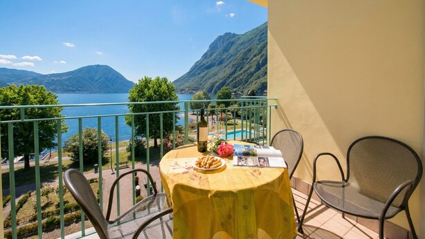A balcony with a table, chairs, a bottle, glasses, and a plate of snacks. - Porto Letizia T11, Porlezza, Italy (Porlezza)