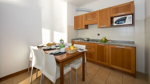 A compact kitchen with wooden cabinets, a microwave, and a dining area with white chairs and a table set for breakfast. - Porto Letizia T11, Porlezza, Italy (Porlezza)