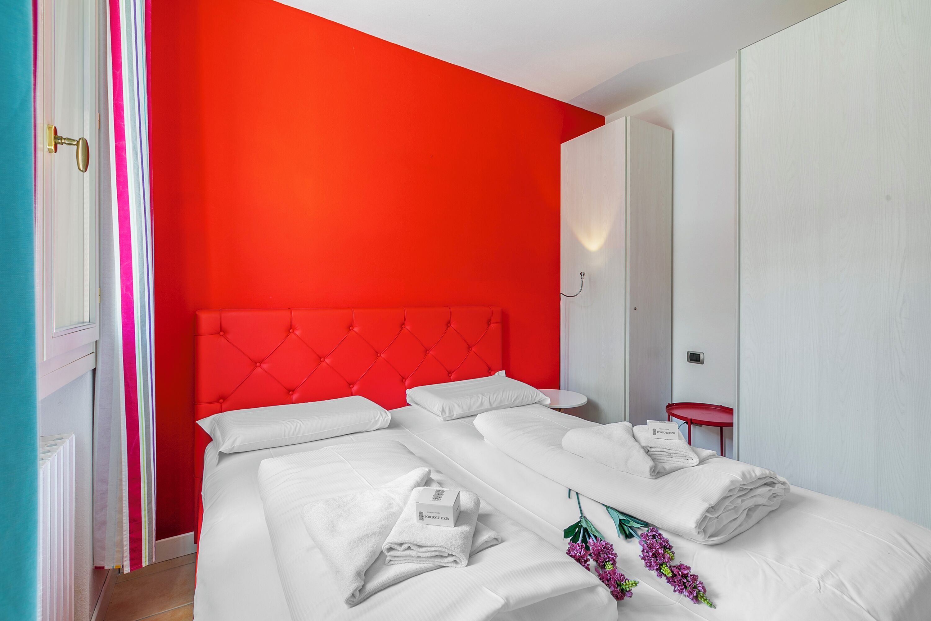 Une chambre d’hôtel avec un mur d’accent rouge, une tête de lit capitonnée et des lits parfaitement faits, recouverts de draps blancs.