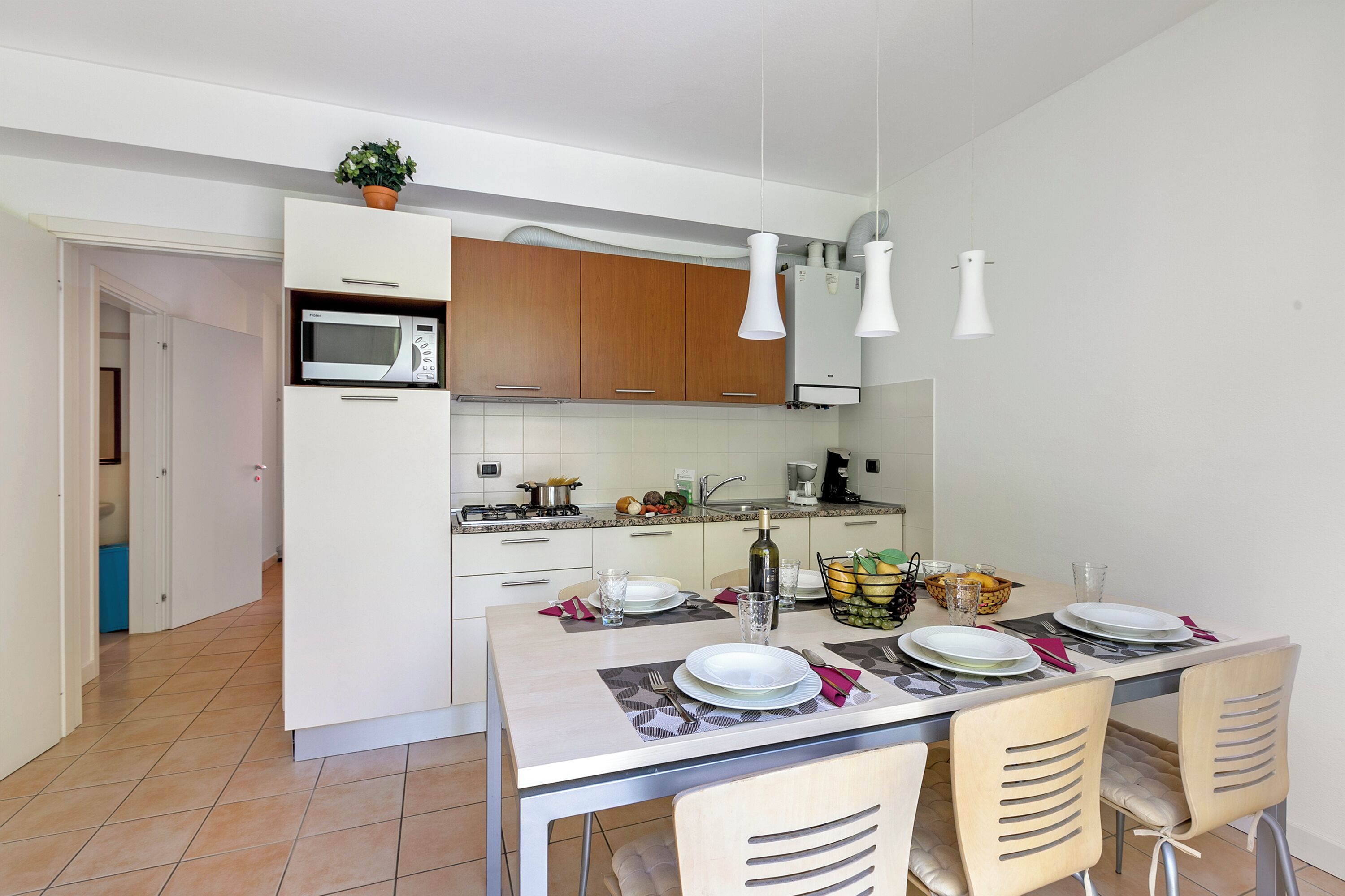 Une cuisine moderne avec des meubles blancs, un four à micro-ondes et un coin repas agrémenté d’assiettes, de verres et d’une bouteille.