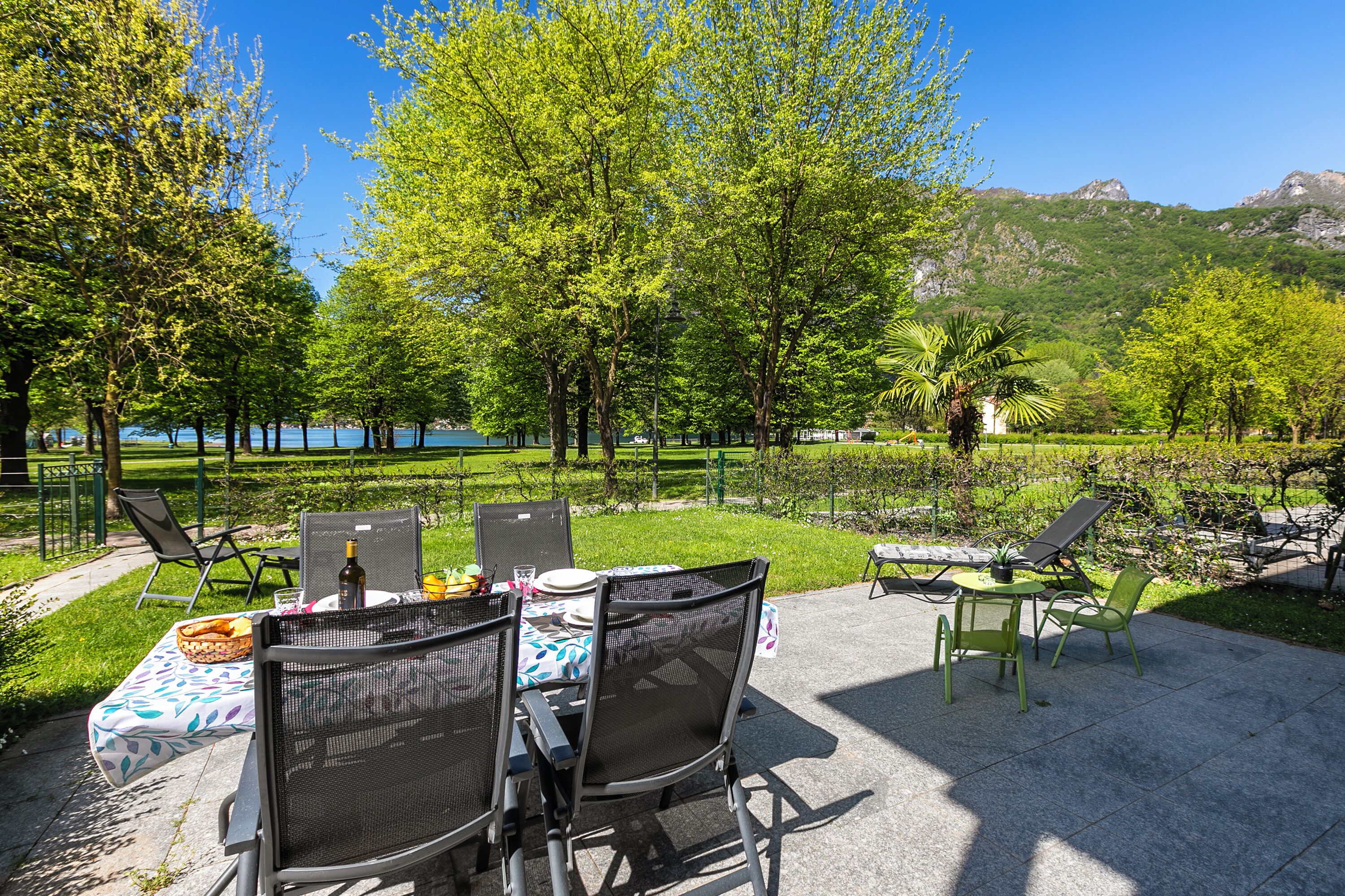 An outdoor dining area with tables and chairs, a view of a lake, and trees.