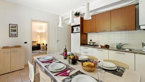 A modern kitchen with white cabinets, a dining area with a table set for four, and a visible microwave. - Porto Letizia Iris 1, Porlezza, Italy (Porlezza)