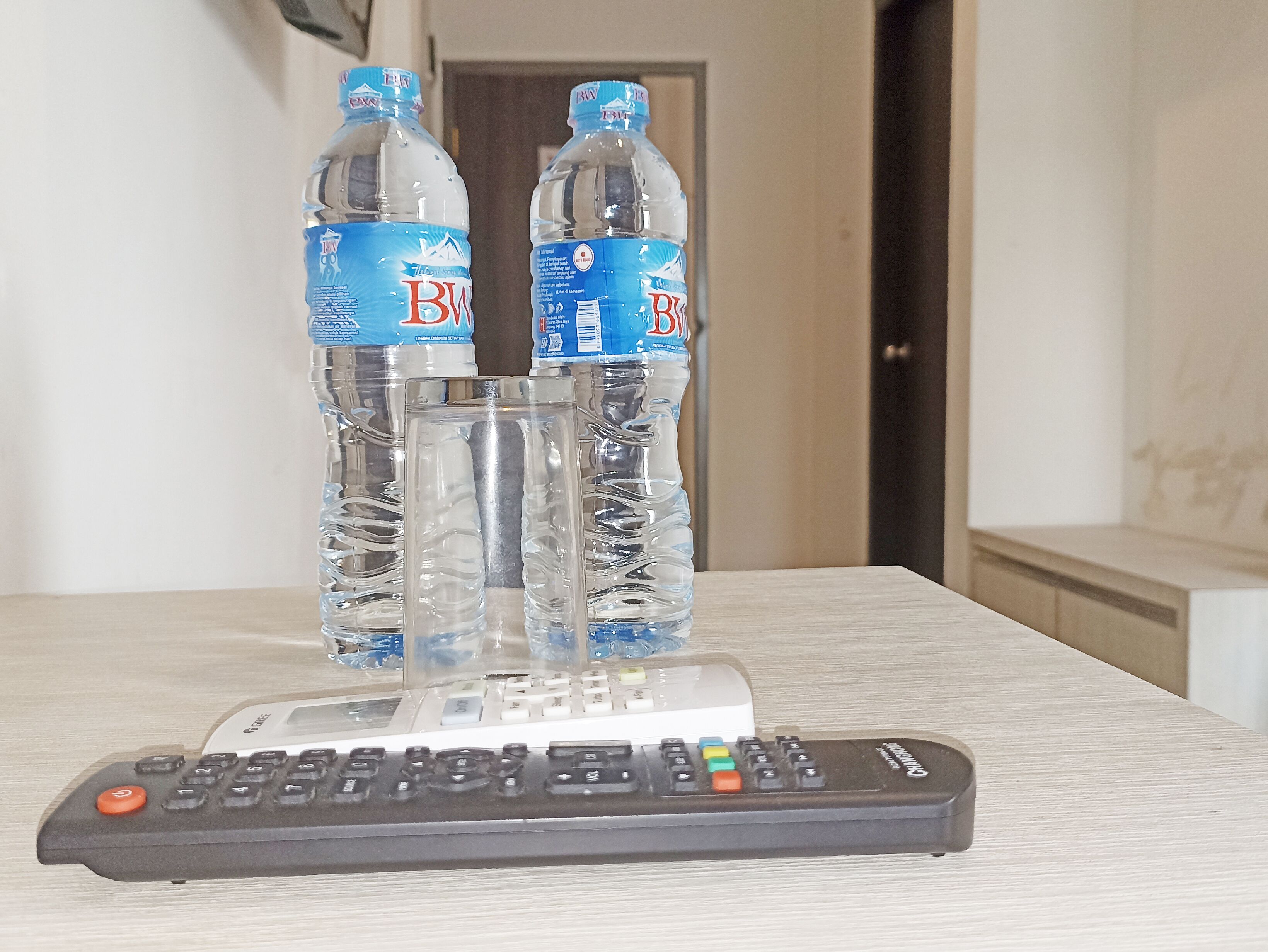 A remote control, two water bottles, and a glass on a table.
