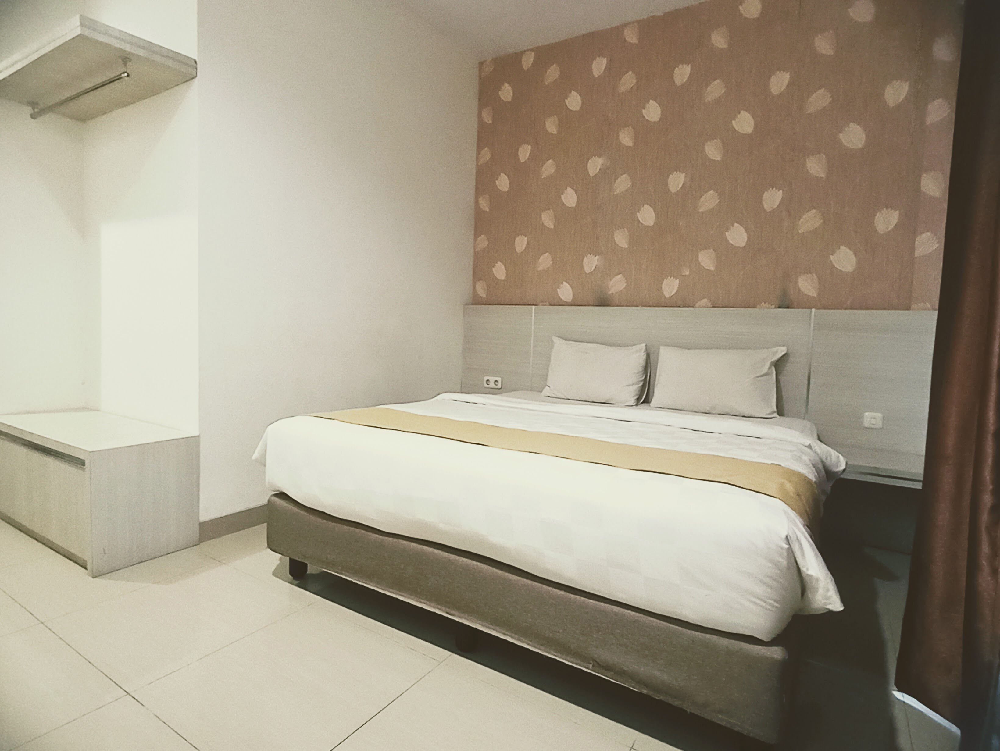 A bedroom with a bed, a headboard, a bedside table, and a wall with a leaf pattern.