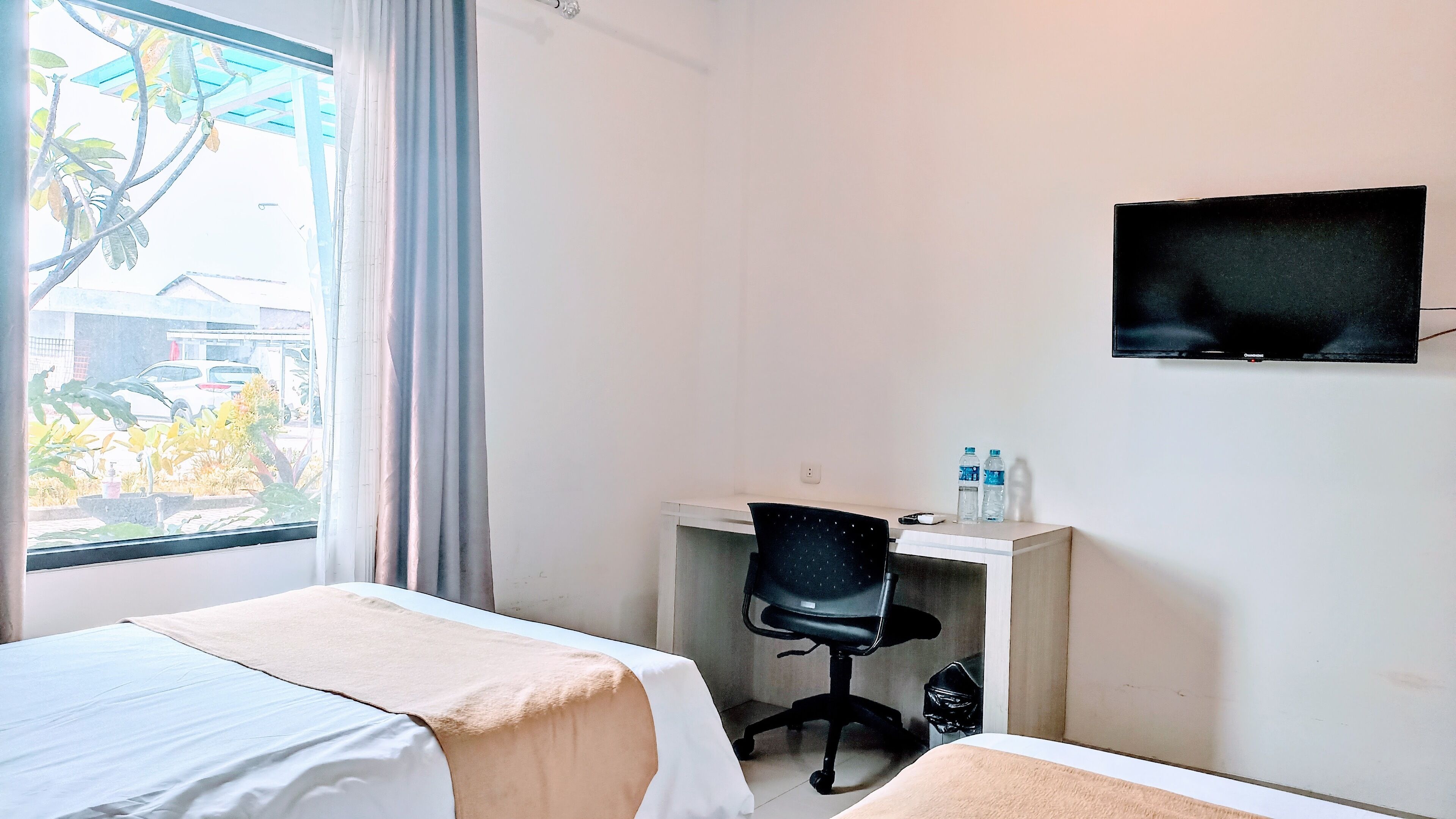 A hotel room with two beds, a desk with a chair, a television, and a window with curtains.