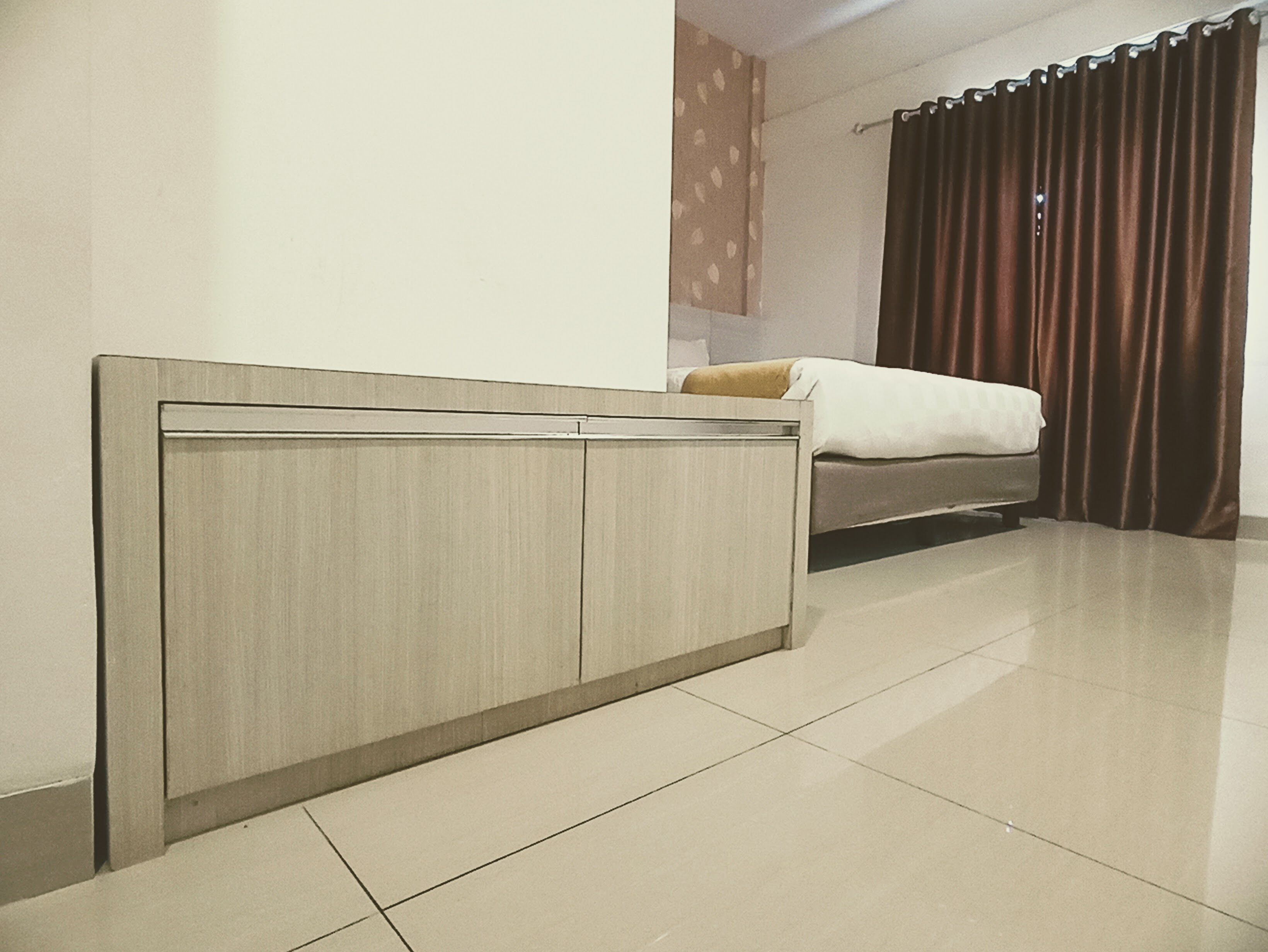 A bedroom with a bed, a headboard, and a curtain.