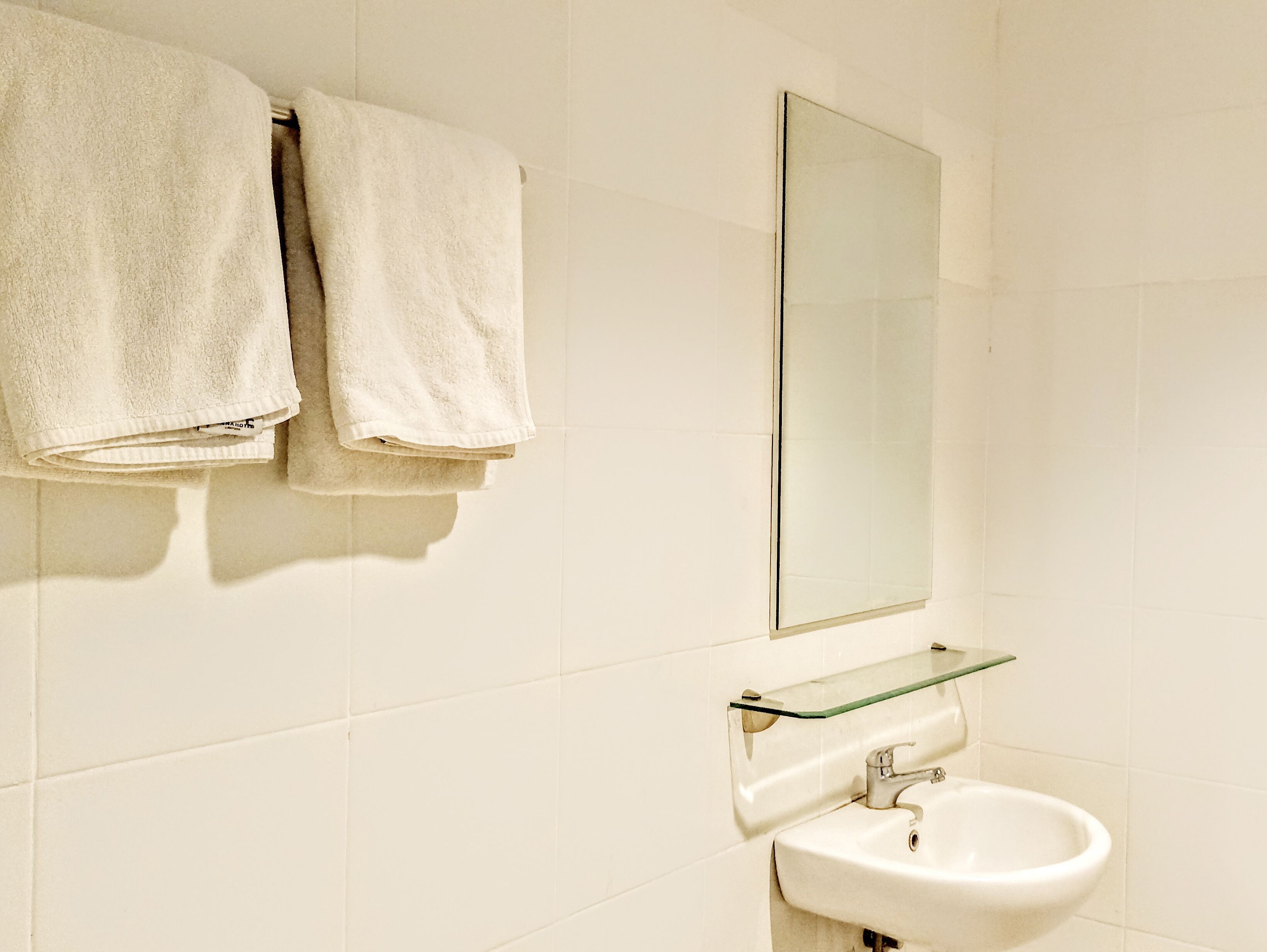 A bathroom with two white towels hanging on a towel rack, a glass shelf above a white sink, and a mirror on the wall.
