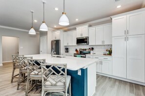 Une cuisine moderne avec des meubles blancs, un îlot central et des luminaires suspendus.