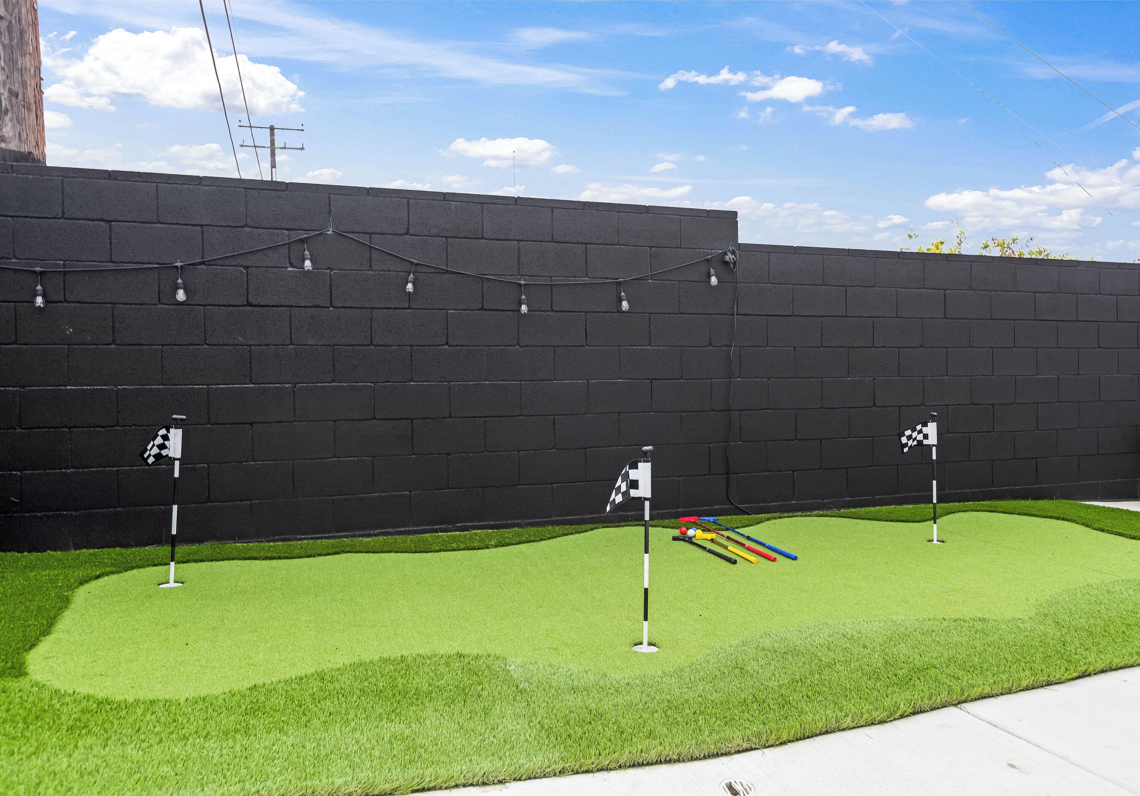 A miniature golf course with artificial grass, a black brick wall, and a clear sky.