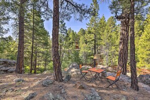 A forested area with a wooden table and chairs, surrounded by large trees and rocks. - Woodsy Flagstaff Hideaway w/ Deck + Sunroom! (Flagstaff)