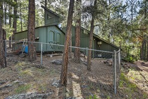 A rustic cabin surrounded by tall pine trees, with a metal fence in the foreground. - Woodsy Flagstaff Hideaway w/ Deck + Sunroom! (Flagstaff)