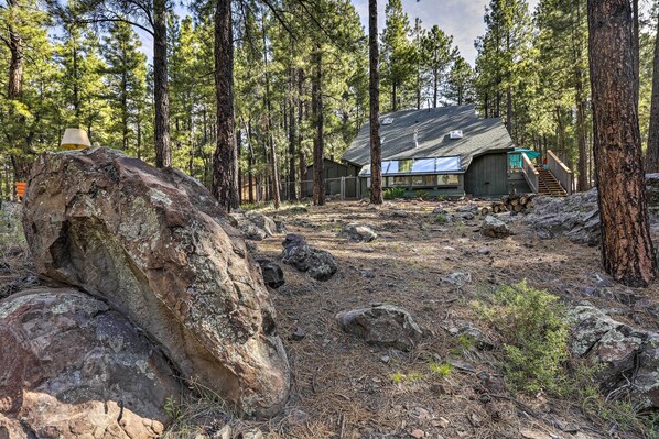 A cabin in a forest with a large rock in the foreground, a wooden deck, and a staircase leading to the main building. - Woodsy Flagstaff Hideaway w/ Deck + Sunroom! (Flagstaff)
