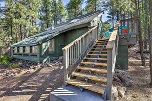 A rustic cabin with a wooden staircase leading to a deck, surrounded by a forest. - Woodsy Flagstaff Hideaway w/ Deck + Sunroom! (Flagstaff)