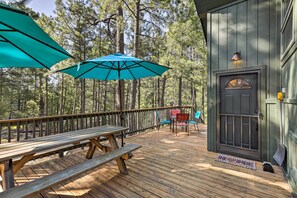 A wooden deck with picnic tables and umbrellas, surrounded by tall pine trees. - Woodsy Flagstaff Hideaway w/ Deck + Sunroom! (Flagstaff)