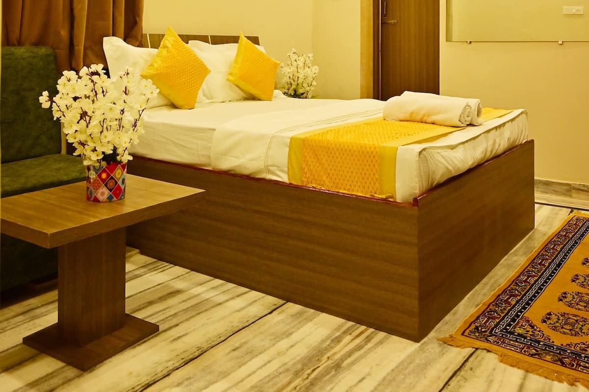 Habitación de hotel con una cama, ventilador de techo, unidad de aire acondicionado, sofá verde, mesa de madera y un jarrón decorativo.