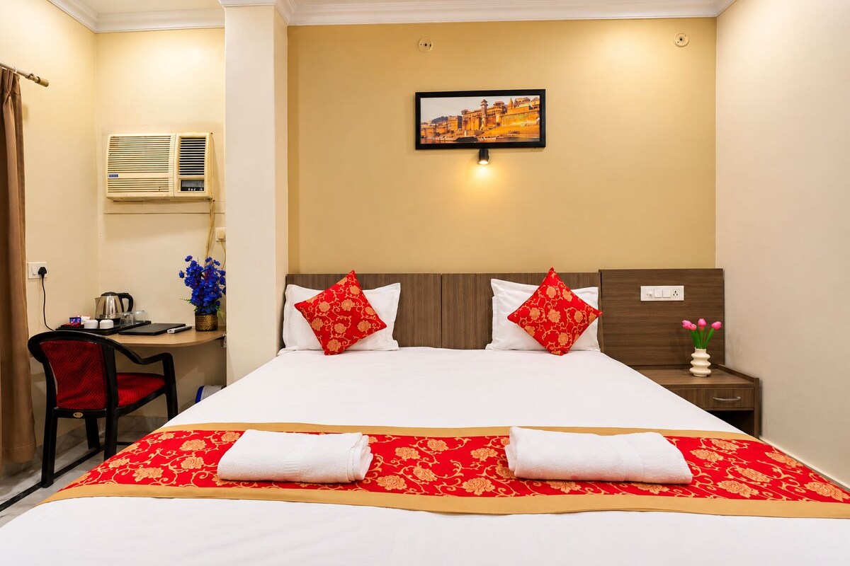A hotel room with a bed, a desk, a chair, a nightstand, and a wall-mounted picture.