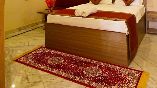 Habitación de hotel con cama, ventilador de techo, aire acondicionado, espejo y alfombra roja.