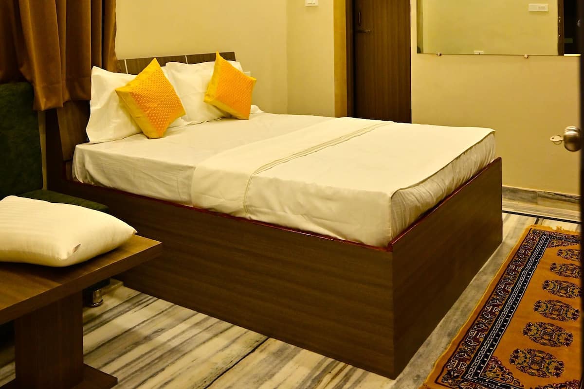 Habitación de hotel con cama, ventilador de techo, equipo de aire acondicionado, puerta, espejo y alfombra estampada.