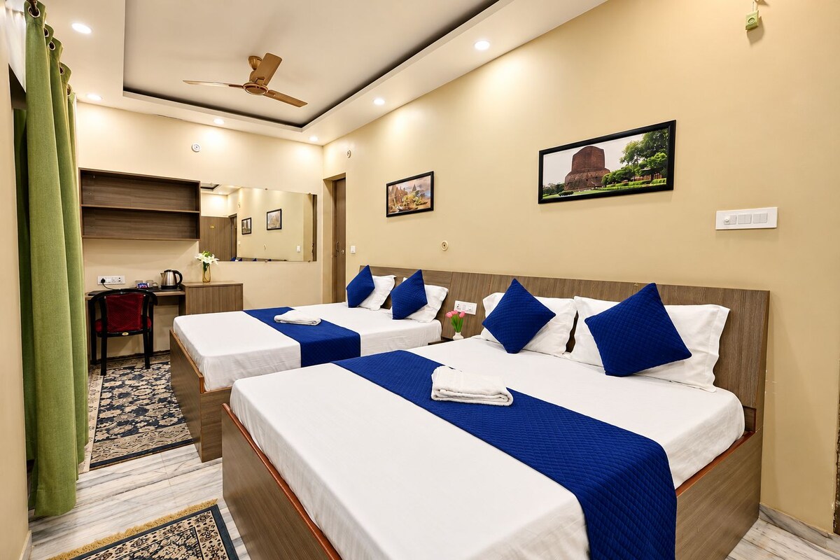 A hotel room with three beds, a desk, a chair, a ceiling fan, and a framed picture on the wall.