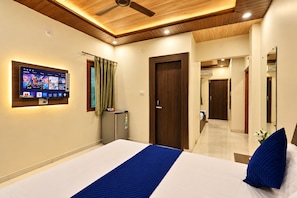 A hotel room with a bed, a television mounted on the wall, a small refrigerator, and a door leading to another room. - Hotel Get Dreams Inn, Varanasi (Varanasi)