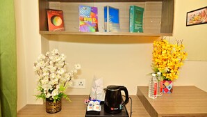 Un escritorio ordenado con una cafetera, dos botellas de agua, una caja de pañuelos y dos jarrones con flores.