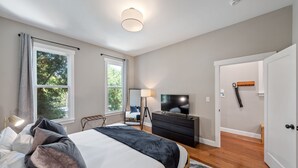 A bedroom with a large bed, a TV, a dresser, and a window with curtains. - / Luxury Modern Home in Oakland with AC & WFH / (Oakland)